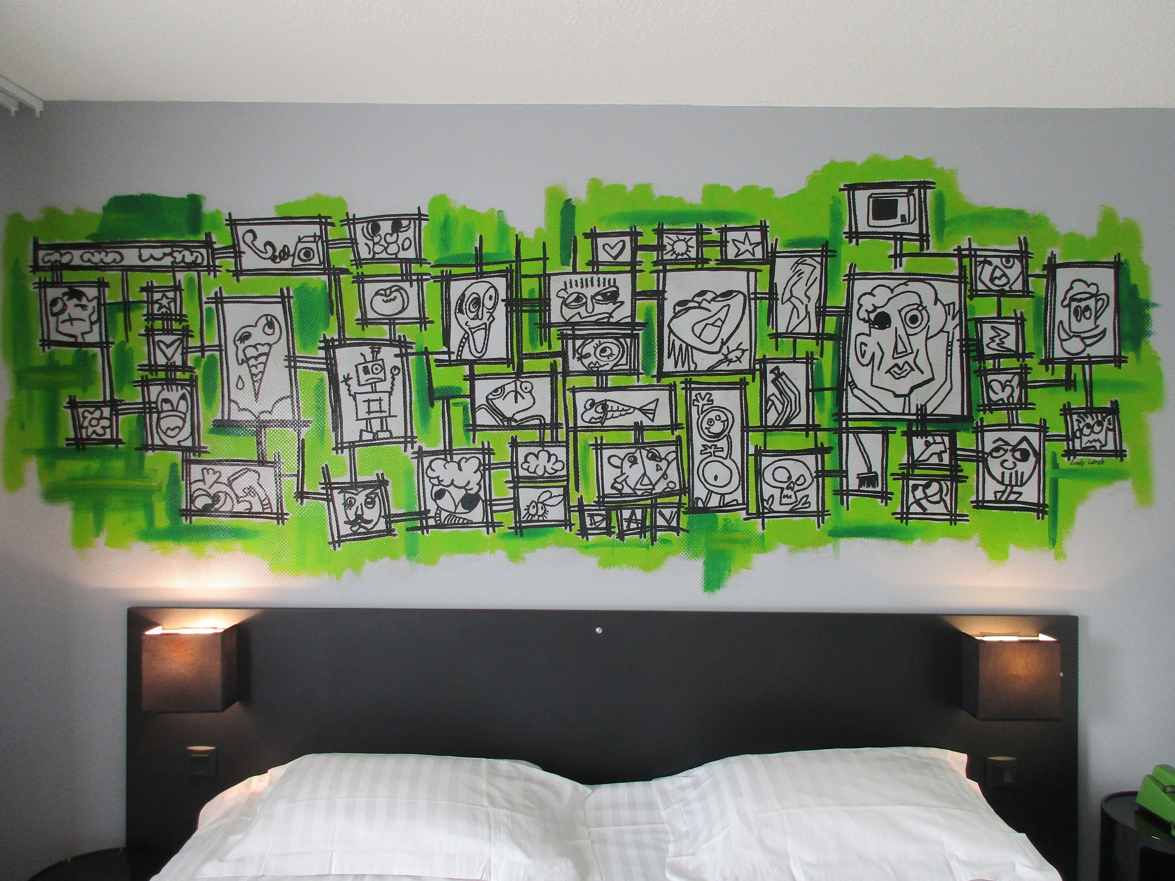 Quarto com uma cama grande, duas luminárias de cabeceira e uma parede decorada com vários desenhos emoldurados.