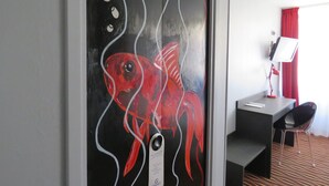 A room with a painting of a red fish on the wall, a desk, a chair, and a TV on the desk. - Citotel Dav'hotel Jaude (Clermont-Ferrand)