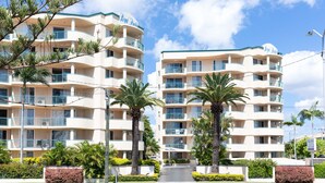 Un hôtel à plusieurs étages doté de balcons, de palmiers et surplombant un ciel dégagé.