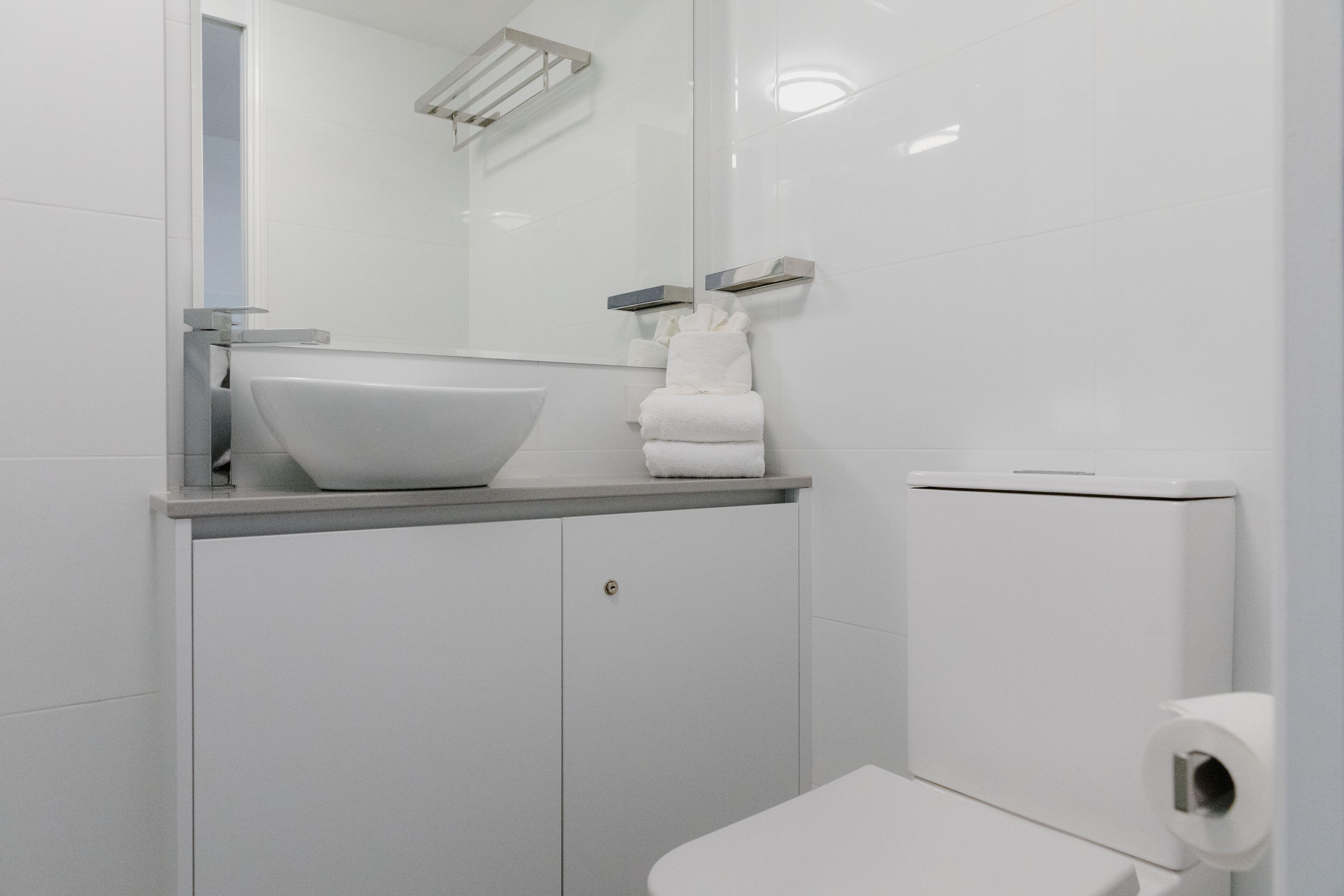 A modern bathroom with a white sink, mirror, and toilet.