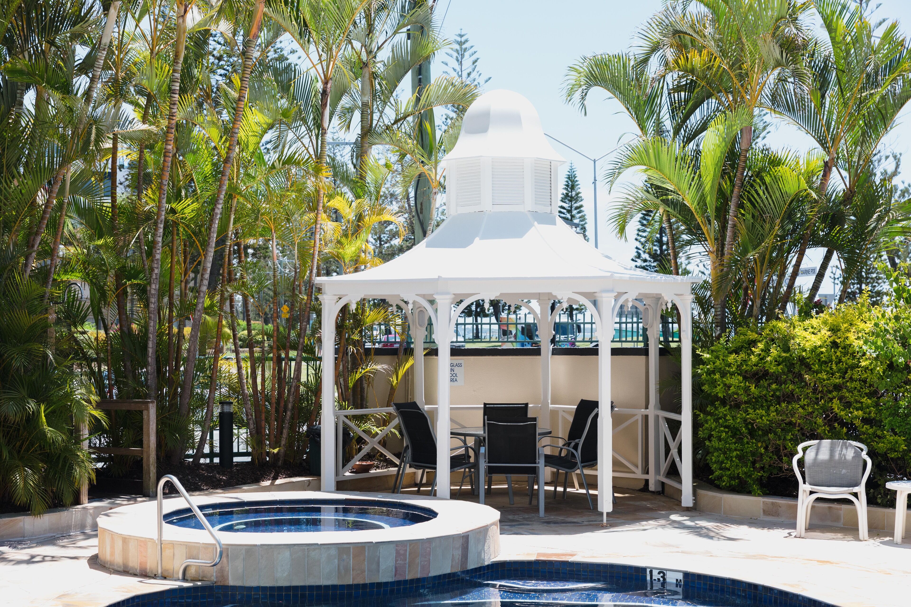 A pool area with a gazebo, lounge chairs, and a small table.