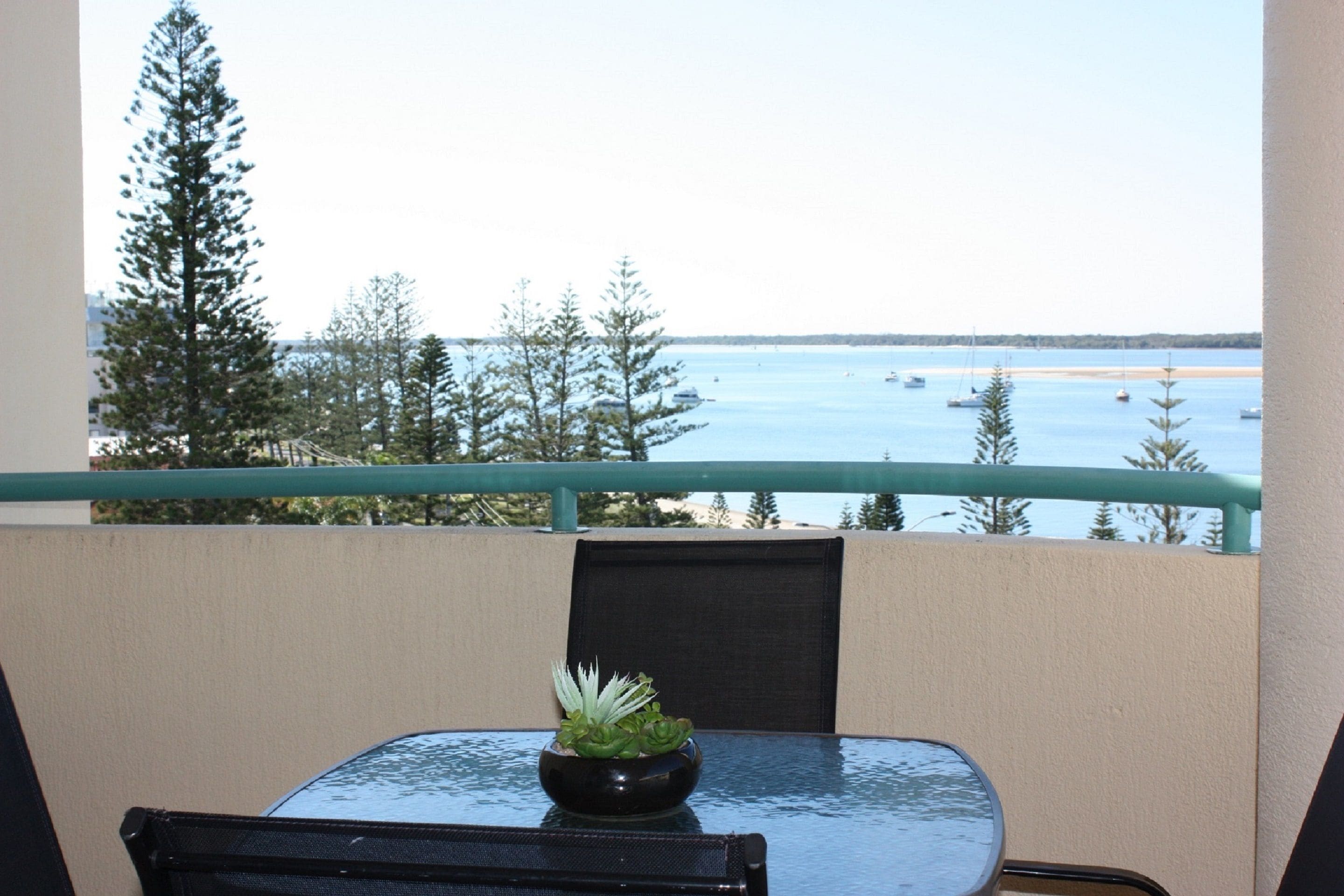 A balcony with a table, a potted plant, and a view of the sea and boats.