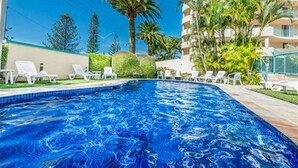Une piscine à l’eau d’un bleu cristallin, entourée de chaises longues blanches et de palmiers.