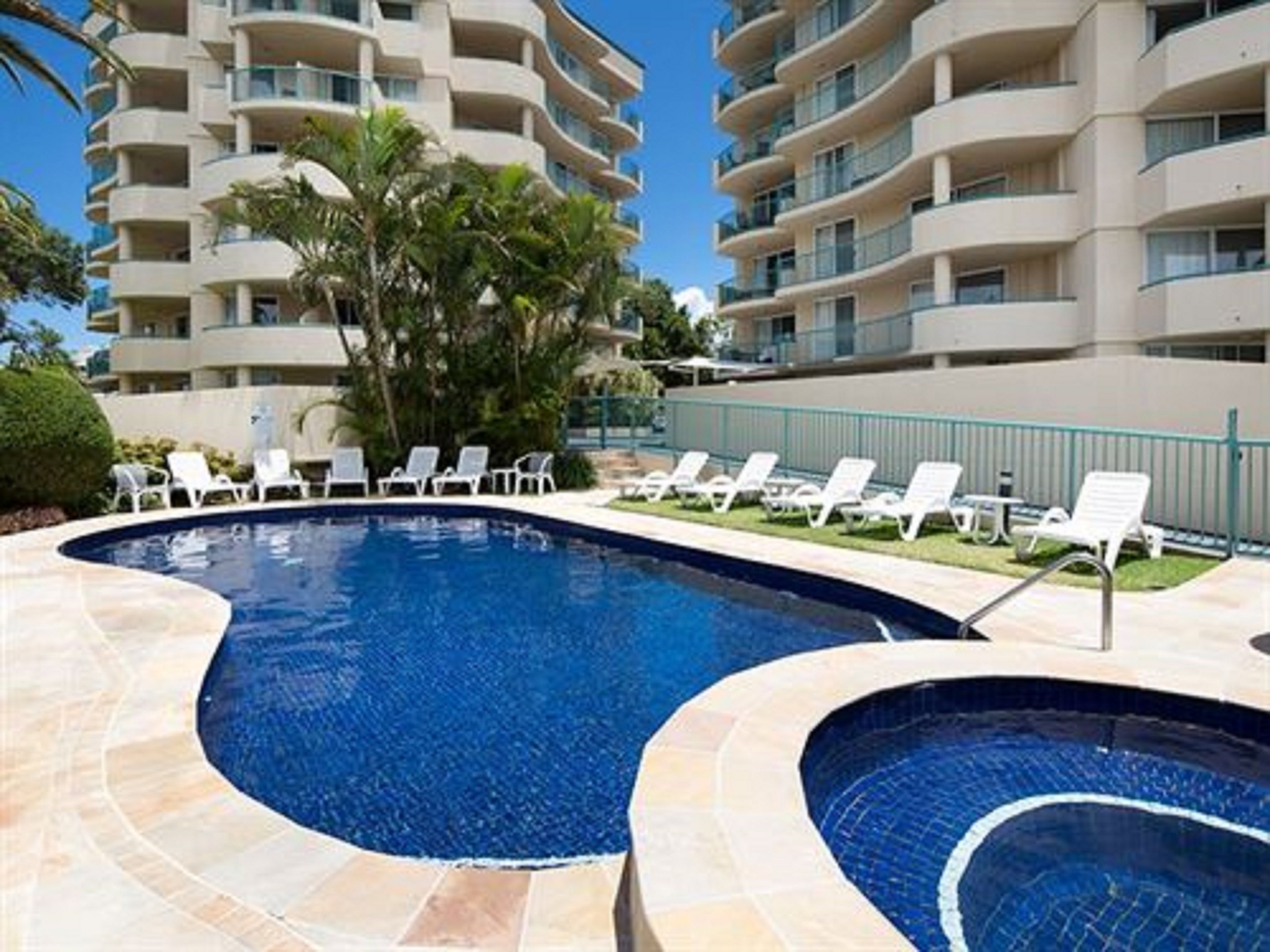 A swimming pool with lounge chairs and a multi-story building in the background.