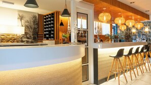 A modern bar area with a curved counter, multiple hanging light fixtures, and a row of bar stools. - Hotel Don Diego (Suances)