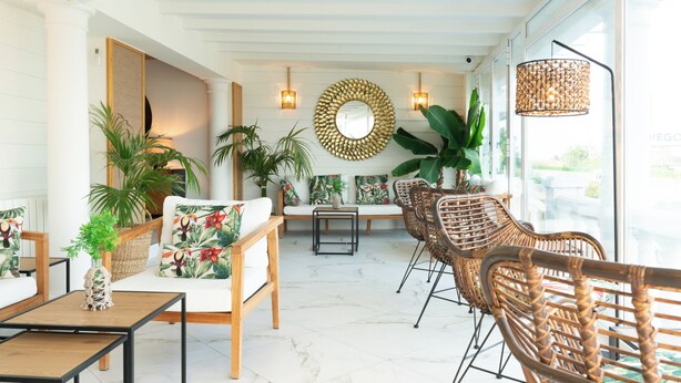 A spacious living area with a white sofa, wicker chairs, a coffee table, and a large mirror on the wall. - Hotel Don Diego (Suances)