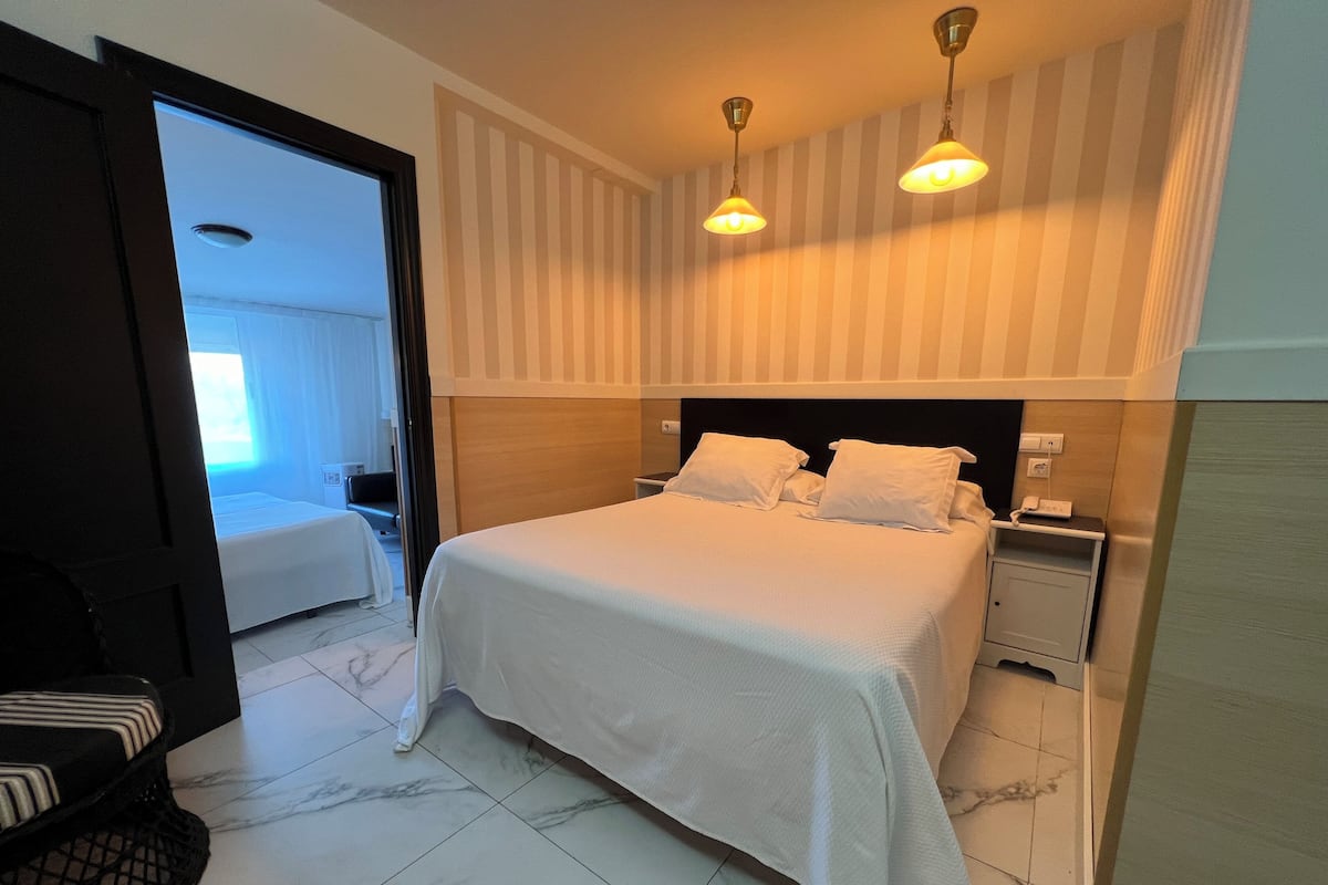 A hotel room with a bed, bedside tables, and a door leading to another room.