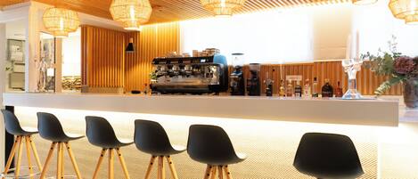 A modern bar area with wooden slatted ceiling, black bar stools, and a coffee machine.