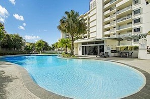 A swimming pool surrounded by a building with balconies and a covered area with seating. - Horton Apartments (Maroochydore)