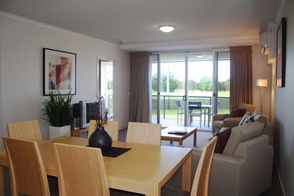 Habitación de hotel moderna con comedor, sofá y balcón con vistas al exterior.