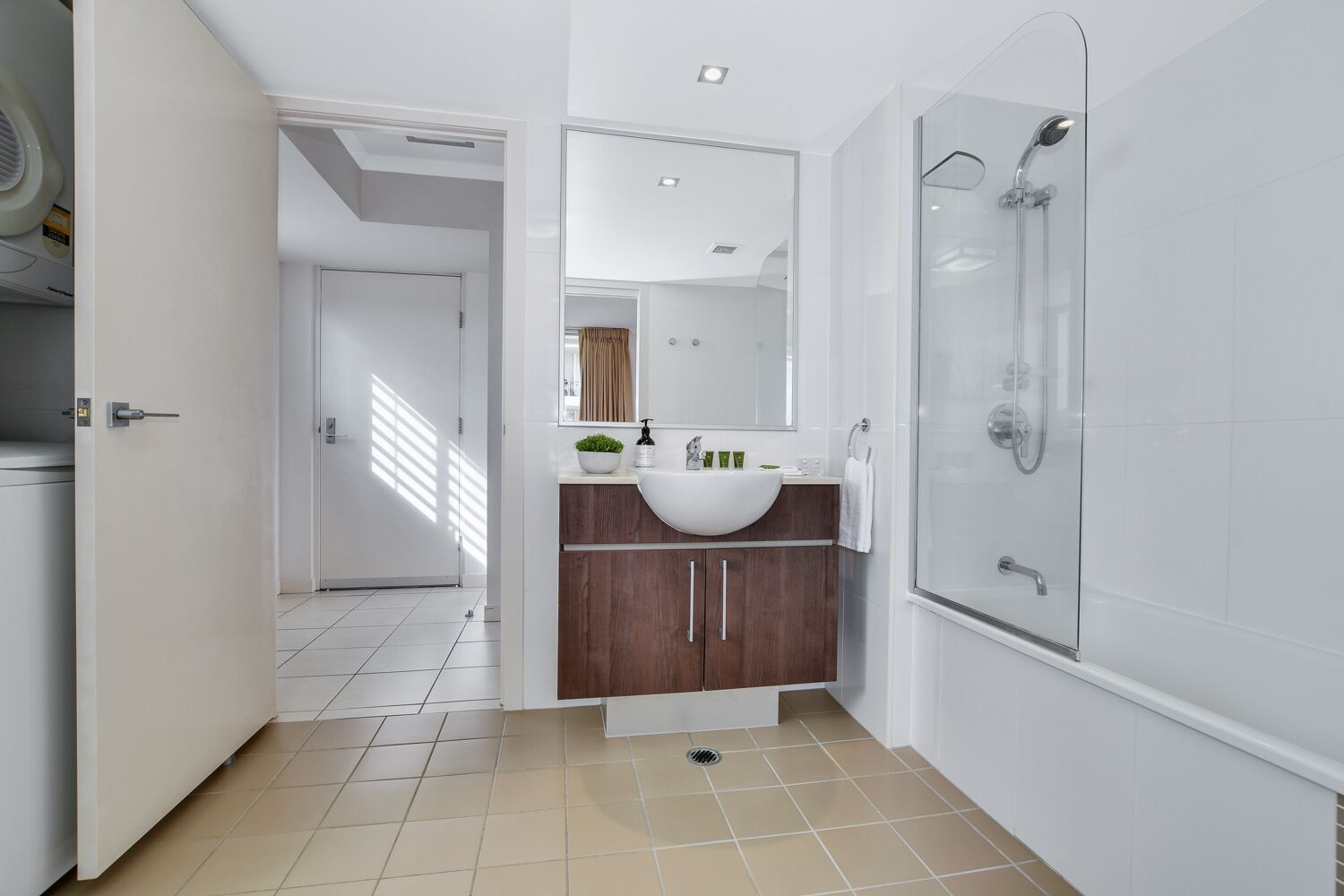 A modern bathroom with a glass shower, a white sink, and a wooden vanity.