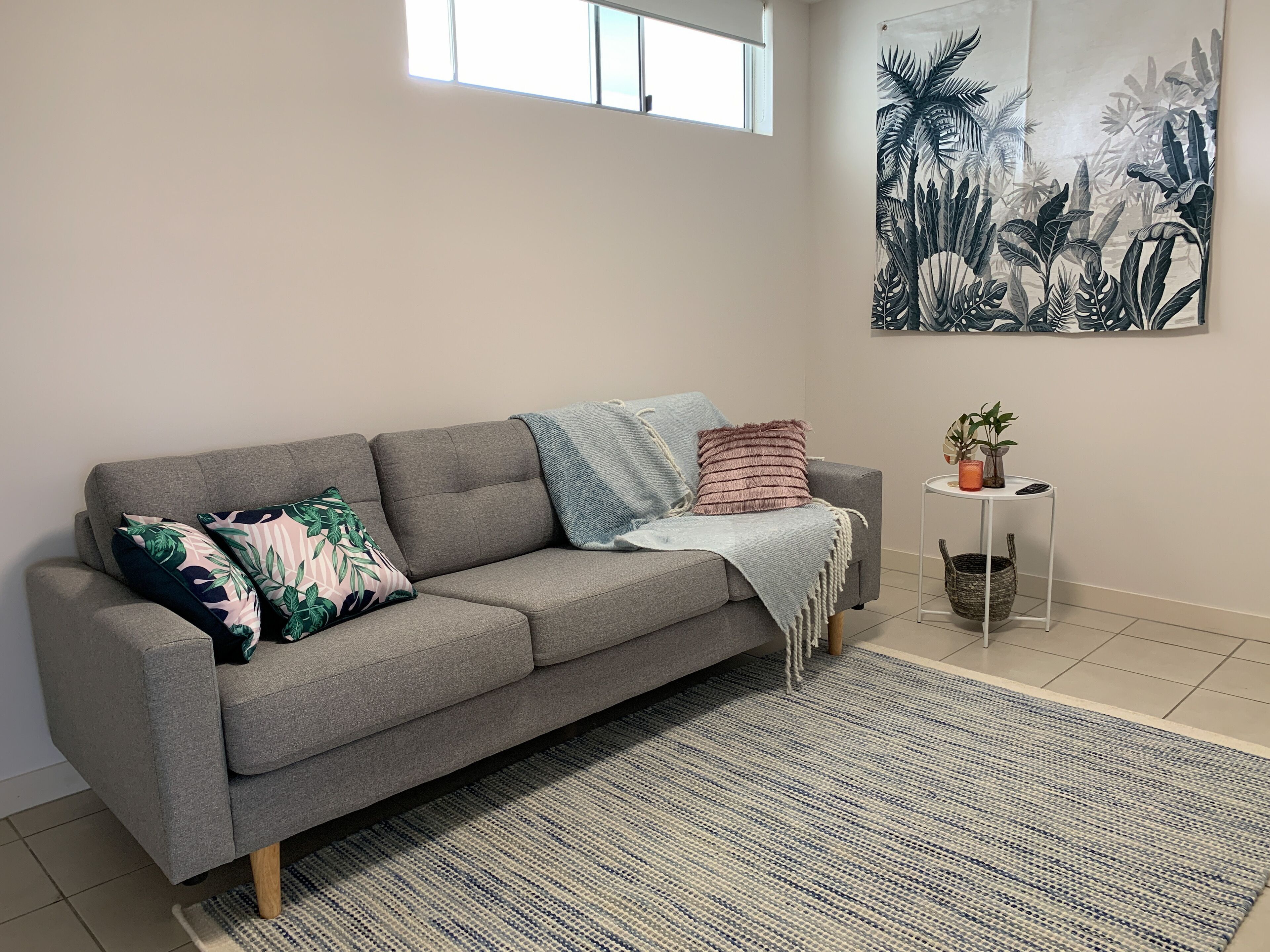 A grey sofa with multiple cushions, a blue and white striped rug, and a small side table with a plant and a glass.