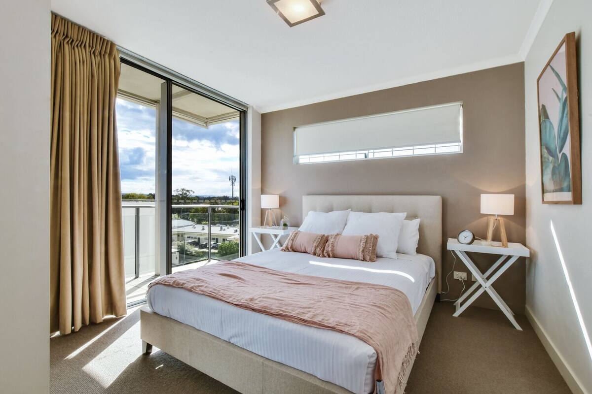 A modern hotel room with a large bed, a view of the city, and a balcony with curtains.