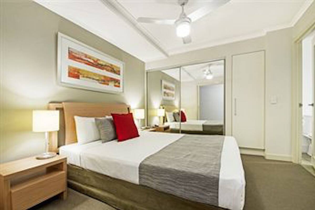 A hotel room with a bed, nightstand, lamp, and a ceiling fan.