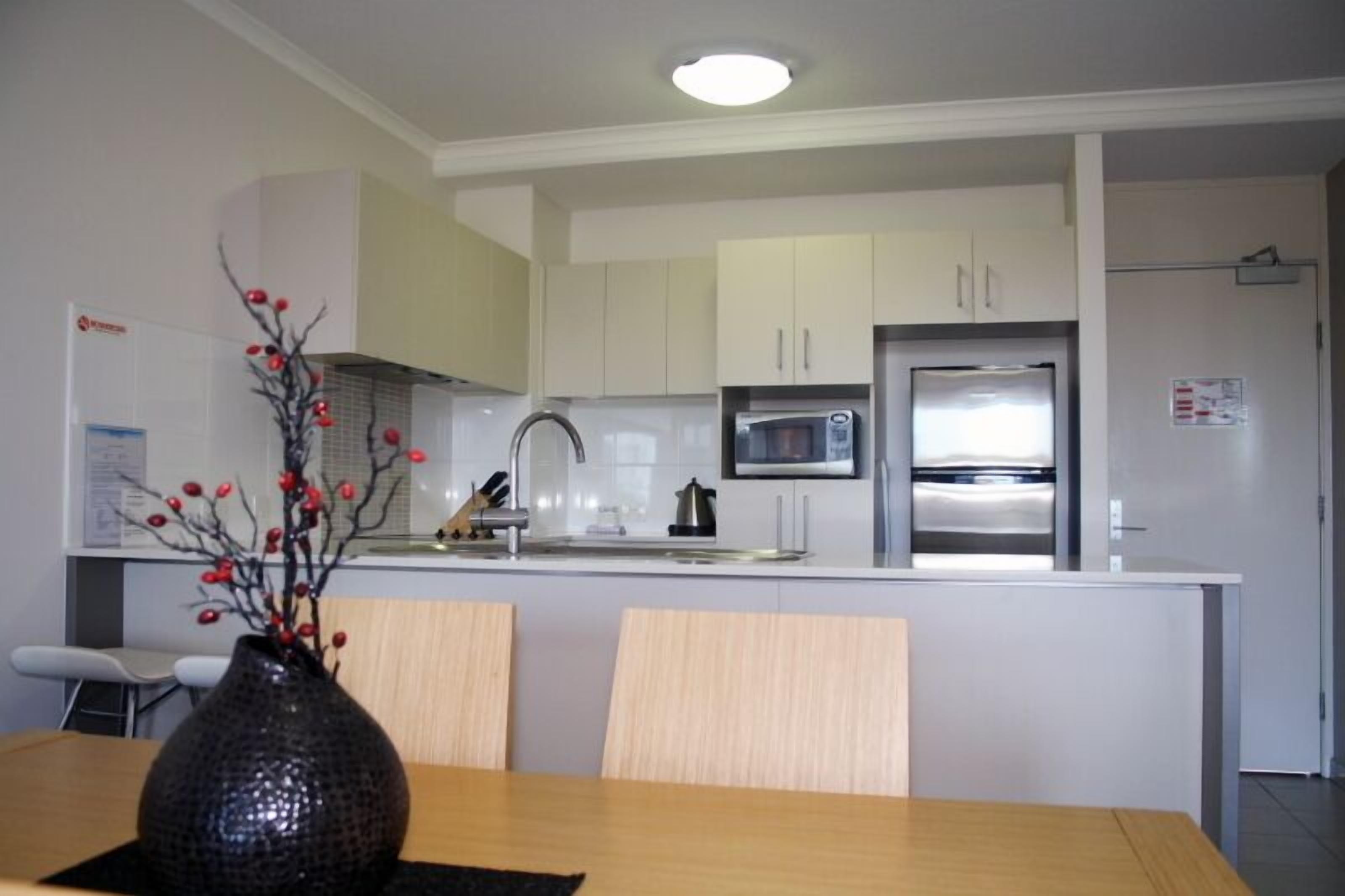 A modern kitchen with white cabinets, a stainless steel refrigerator, a microwave, and a sink.