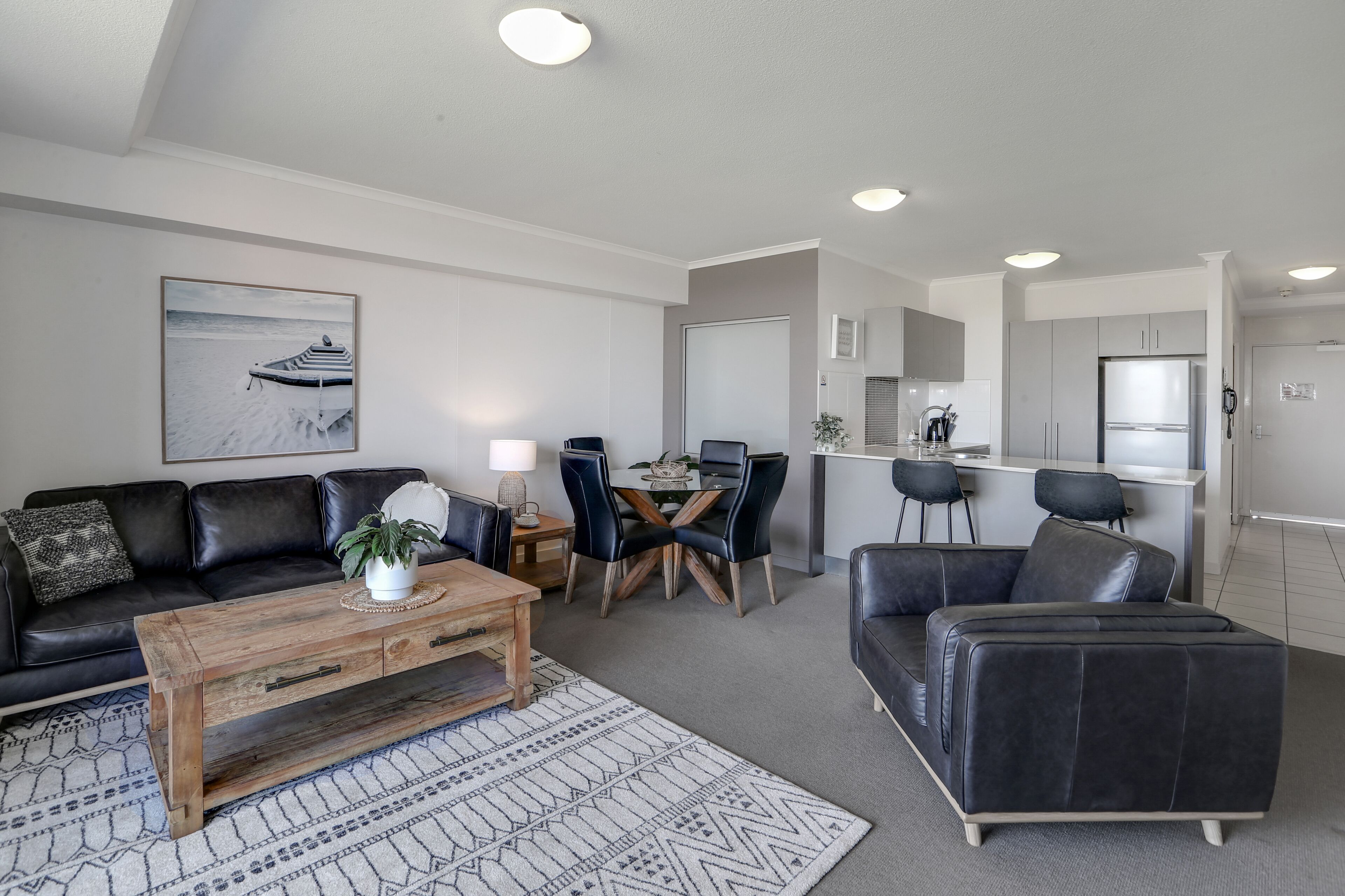 Un salon moderne avec un canapé en cuir noir, une table basse en bois et un coin repas comprenant une table et des chaises.
