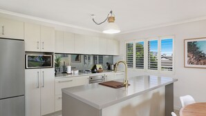Cozinha moderna com ilha central, eletrodomésticos de aço inoxidável e vista para o exterior através de grandes janelas.