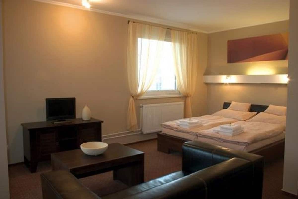 Quarto de hotel com uma cama, televisão, escrivaninha, cadeira e janela com cortinas.