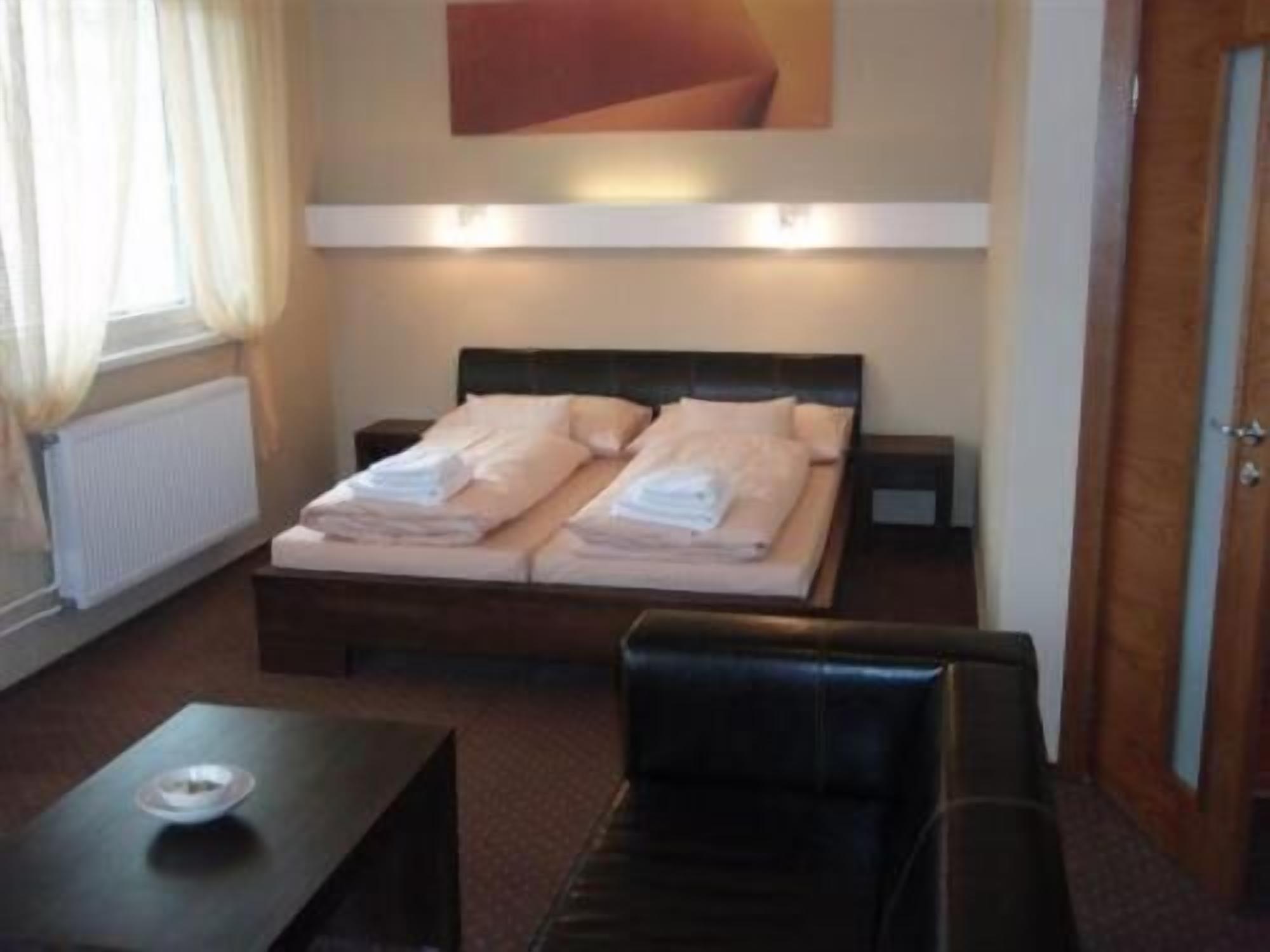 Habitación de hotel con cama, mesitas de noche, una silla, un radiador y una ventana con cortinas.