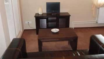 A living room with a dark brown sofa, a small wooden table with a bowl, and a television on a dark wooden cabinet.