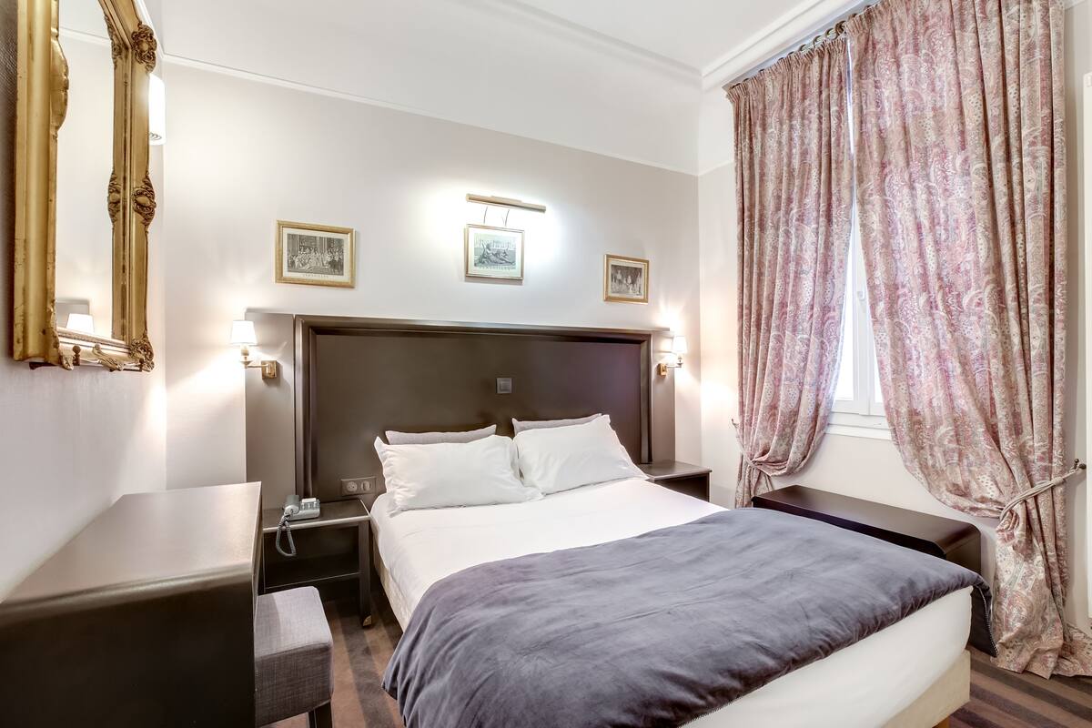 Una habitación de hotel con una cama grande, mesitas de noche, un escritorio y un espejo.