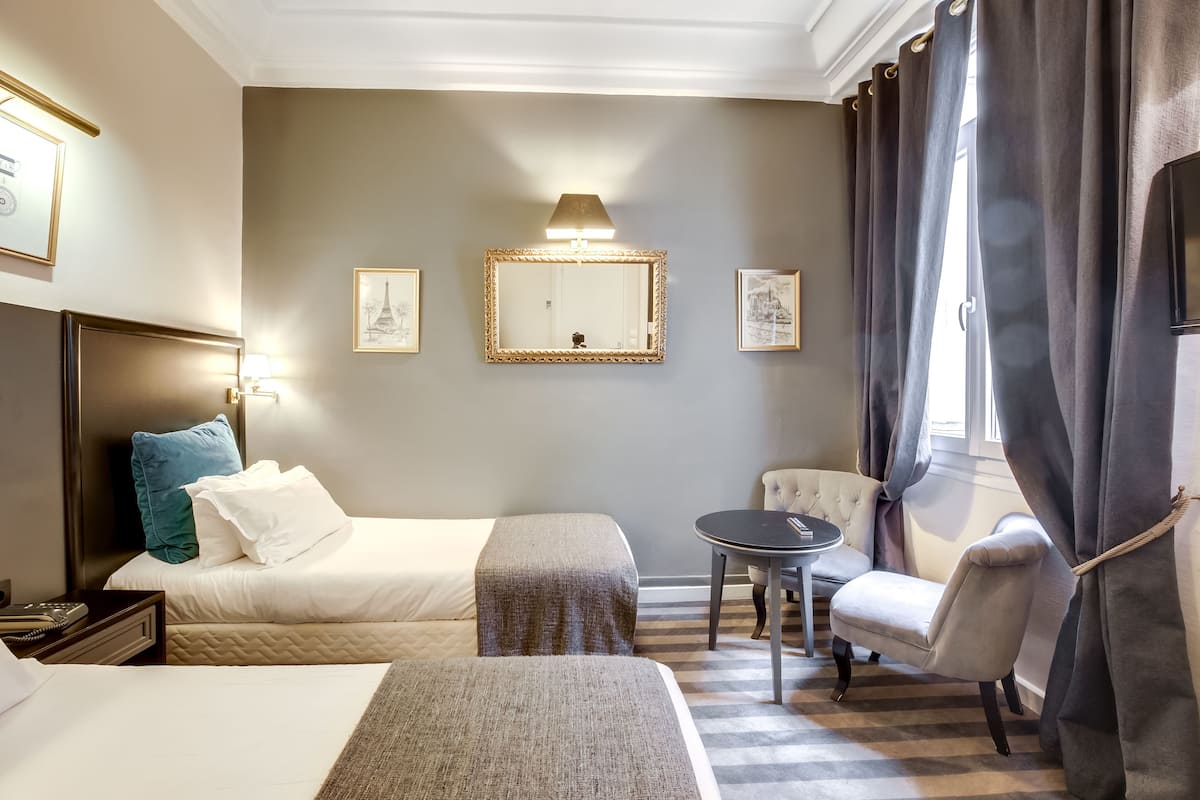 Habitación de hotel con dos camas, una mesita redonda pequeña, una silla, una lámpara y un espejo.