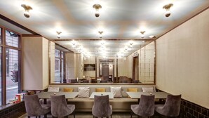 A modern dining area with a long table, cushioned seating, and a large mirror. - Hotel Opéra Maintenon (Paris)