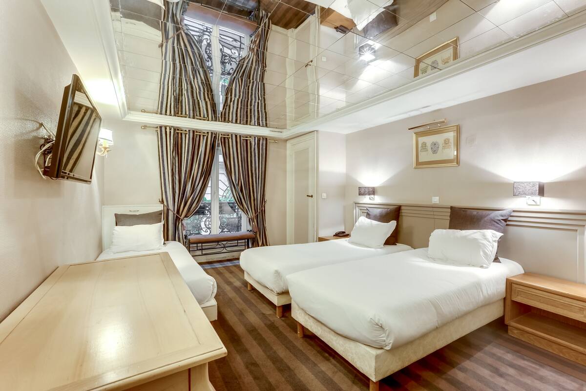 Habitación de hotel con dos camas, una mesita, un banco junto a la ventana y vistas al exterior.
