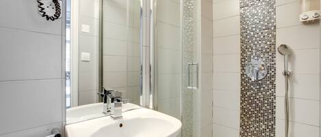 Un baño moderno con ducha envuelta en vidrio, un lavabo blanco y un revestimiento de azulejos en la pared de la ducha.