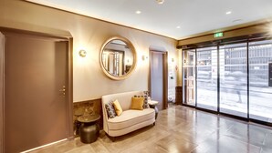 A lobby with a sofa, a round mirror, and a door. - Hotel Opéra Maintenon (Paris)