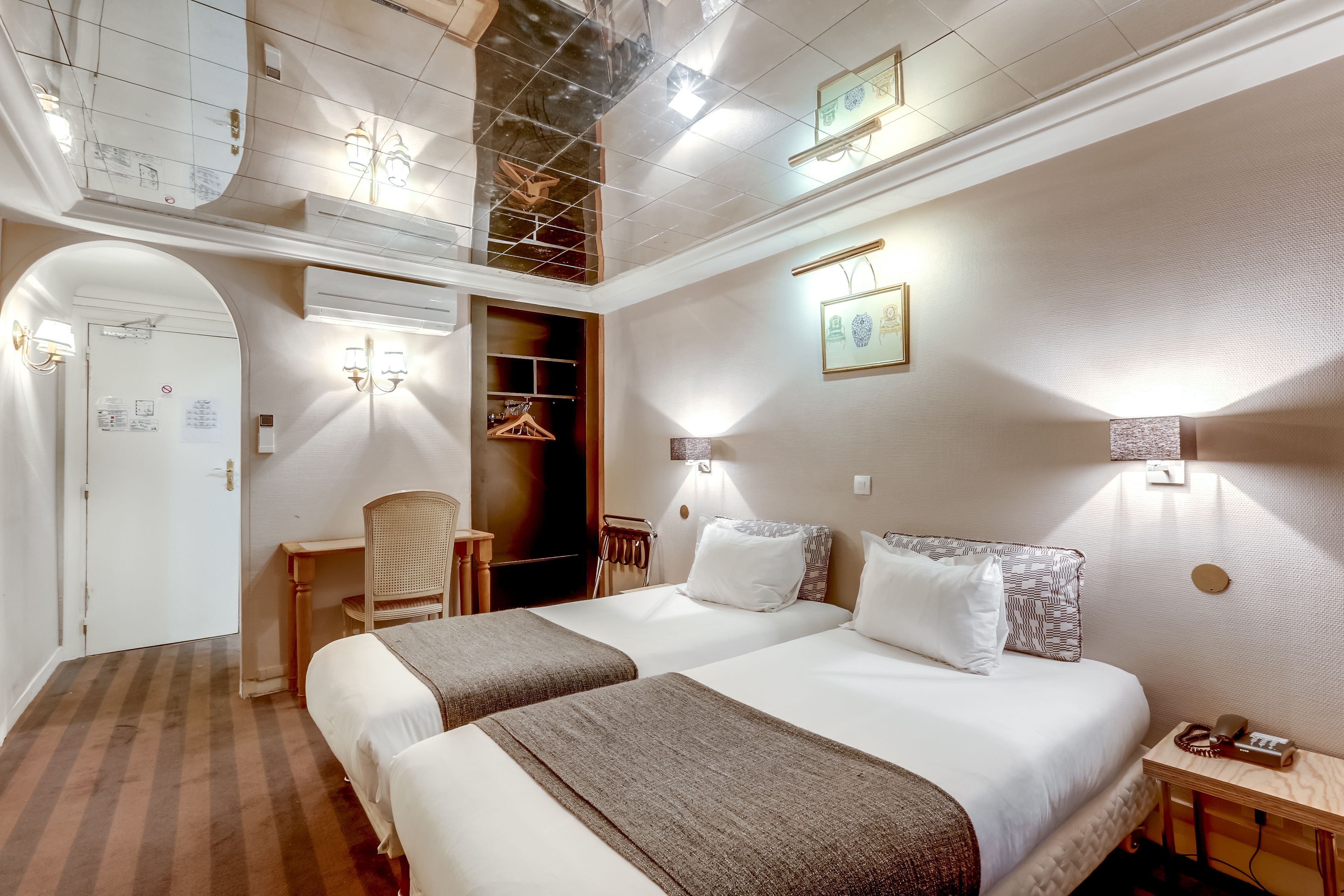 A hotel room with two beds, a desk, a chair, and a wardrobe.