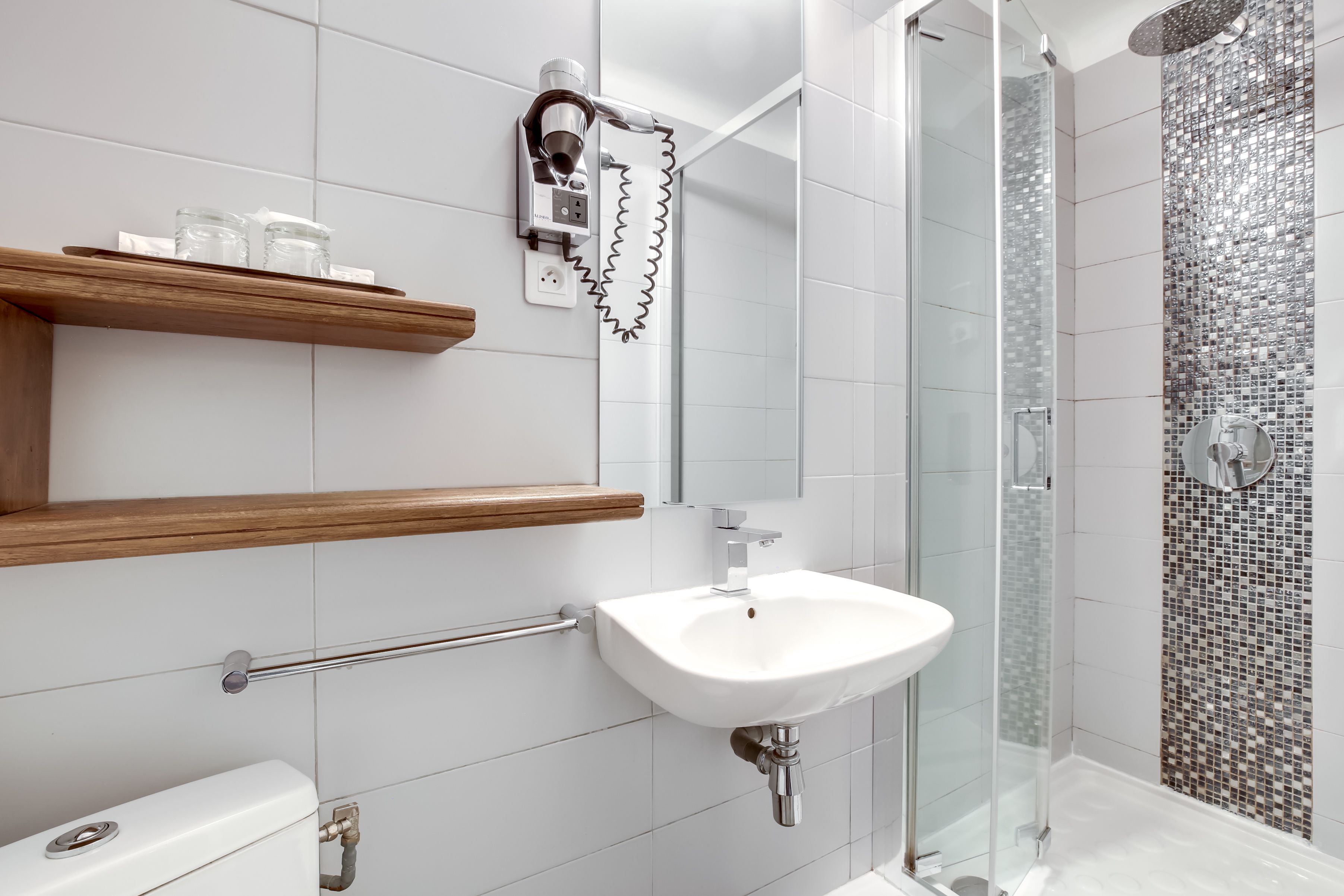 A modern bathroom with a white sink, wooden shelves, a glass shower enclosure, and a tiled shower wall.