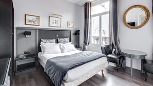 A modern bedroom with a large bed, bedside tables, a desk, a chair, a round table, and a window with curtains. - Hotel Opéra Maintenon (Paris)