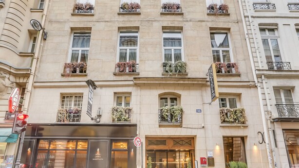 A hotel facade with multiple windows, some with flower boxes, a visible entrance, and a sign indicating it is a hotel. - Hotel Opéra Maintenon (Paris)