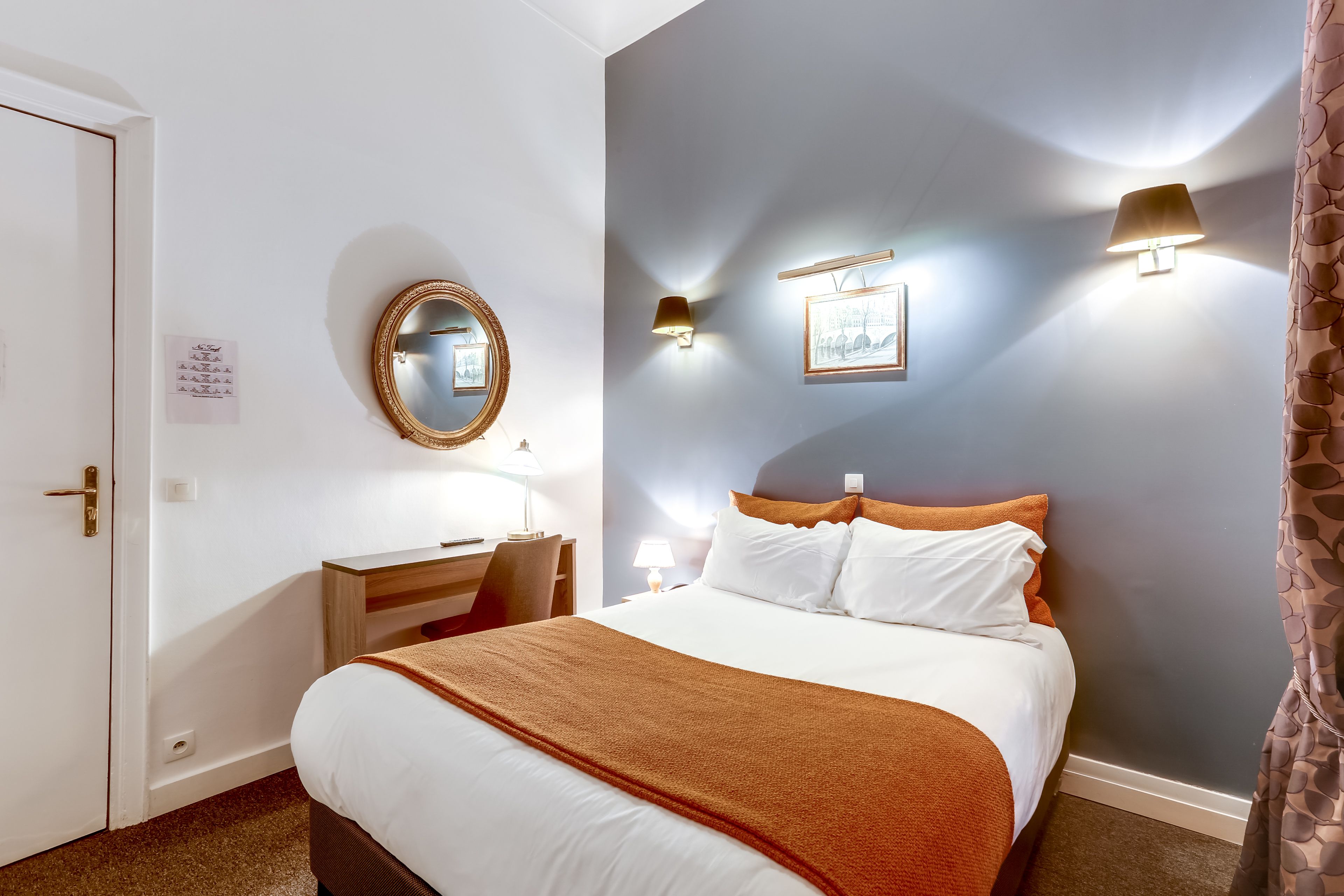 A hotel room with a bed, bedside table, lamp, and a wall-mounted mirror.
