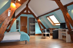 Quarto com teto inclinado, vigas de madeira, cama, escrivaninha, cadeira, televisão e claraboia.