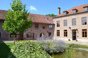 Um edifício de tijolos tradicional, com várias janelas e um pátio com lago e vegetação.