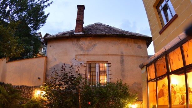 A patio area with a brick floor, outdoor seating, and a building with a tiled roof. - Coroana Brasovului (Brasov)