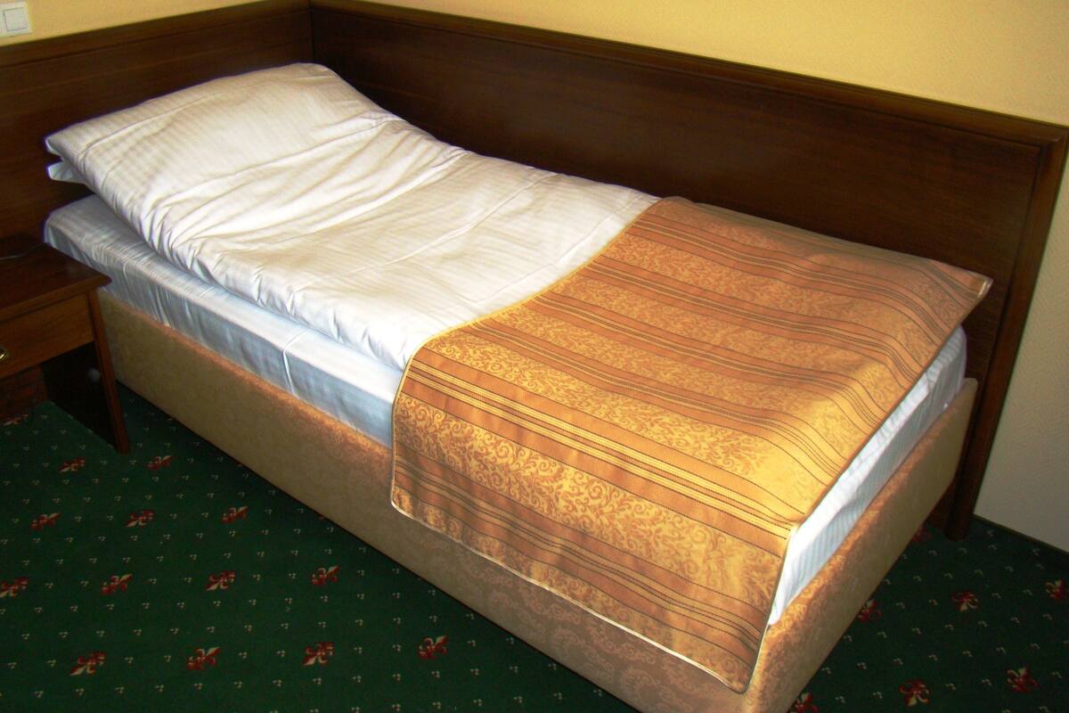 Una cama individual con cabecera de madera, colchón blanco y manta estampada.