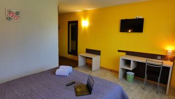 Ein Hotelzimmer mit Bett, Schreibtisch, Stuhl, Fernseher und Lampe.