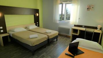 A hotel room with two beds, a desk with a laptop, a window with curtains, and a radiator.