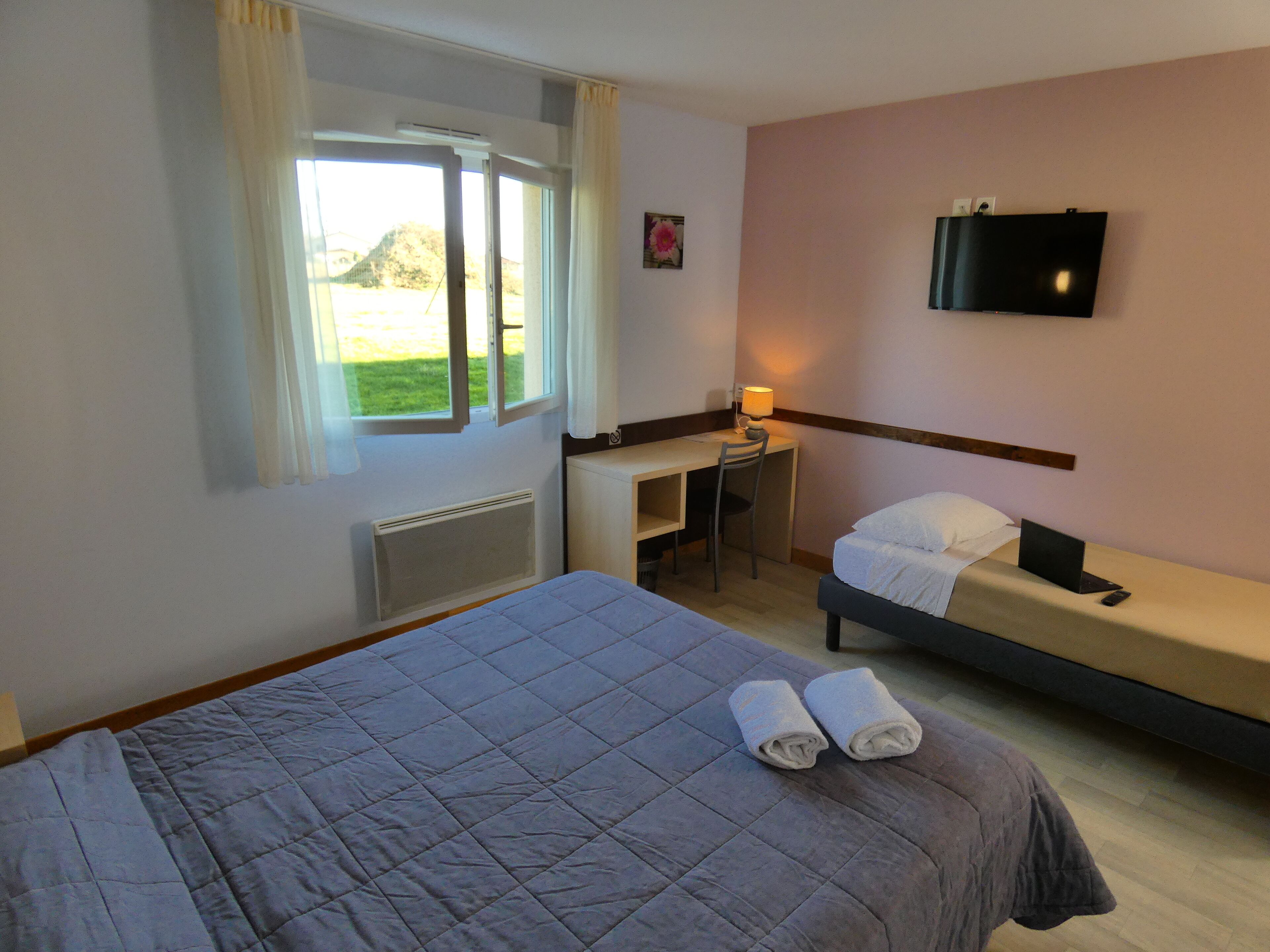 Una habitación de hotel con cama, escritorio, silla, televisor y ventana con cortinas.