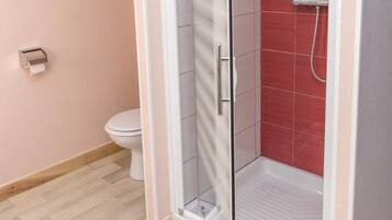 A modern bathroom with a glass-enclosed shower, a toilet, and a pink wall.
