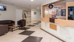 A reception area with a check-in counter, a television, a painting, and a coffee table with magazines.