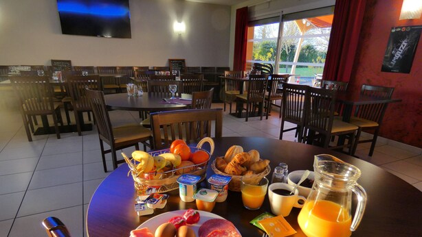 A breakfast setting with a table set for two, featuring croissants, eggs, ham, and a fruit basket.