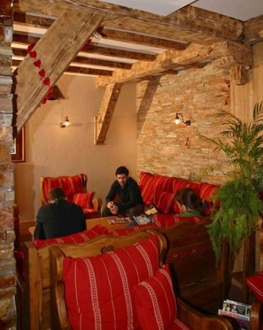 A cozy room with wooden beams, stone walls, and red-striped sofas. - Le Christania (Bellevaux)