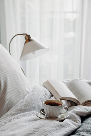 A bed with a white blanket, a cup of coffee, and an open book. - Le Christania (Bellevaux)