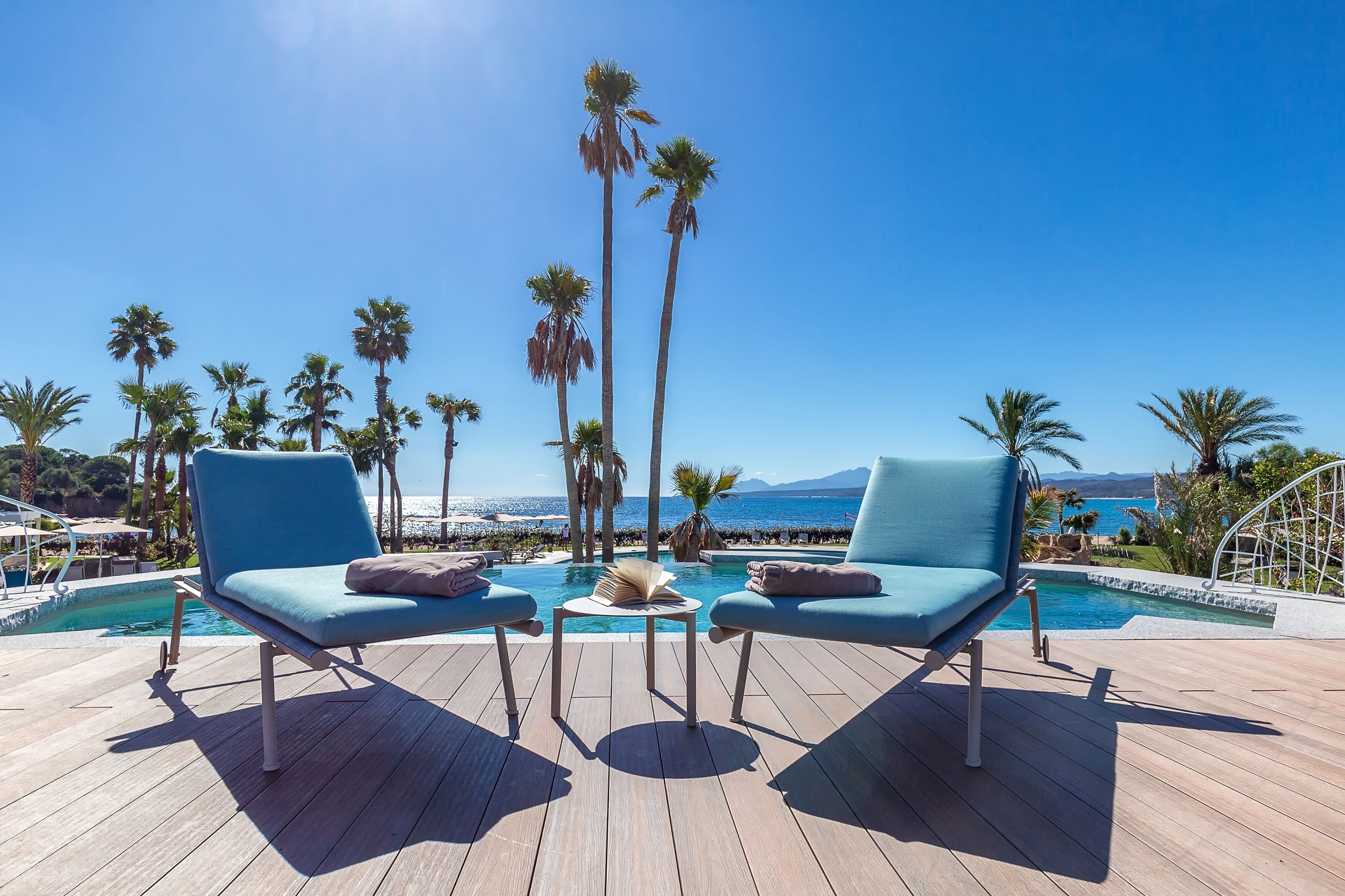 A poolside area with two lounge chairs, a small table, and a book.