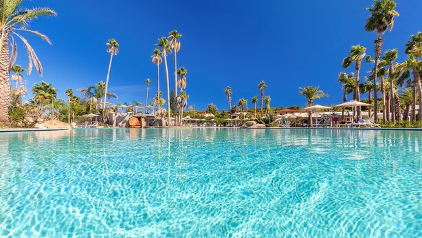 A clear blue pool surrounded by palm trees and umbrellas. - Hotel Club Saraceno (Tortoli)