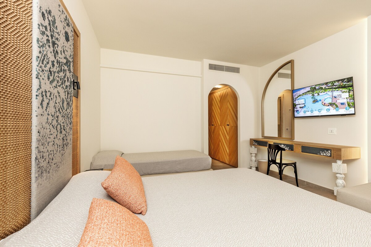 A hotel room with a bed, a desk, a chair, a television, and a wardrobe.